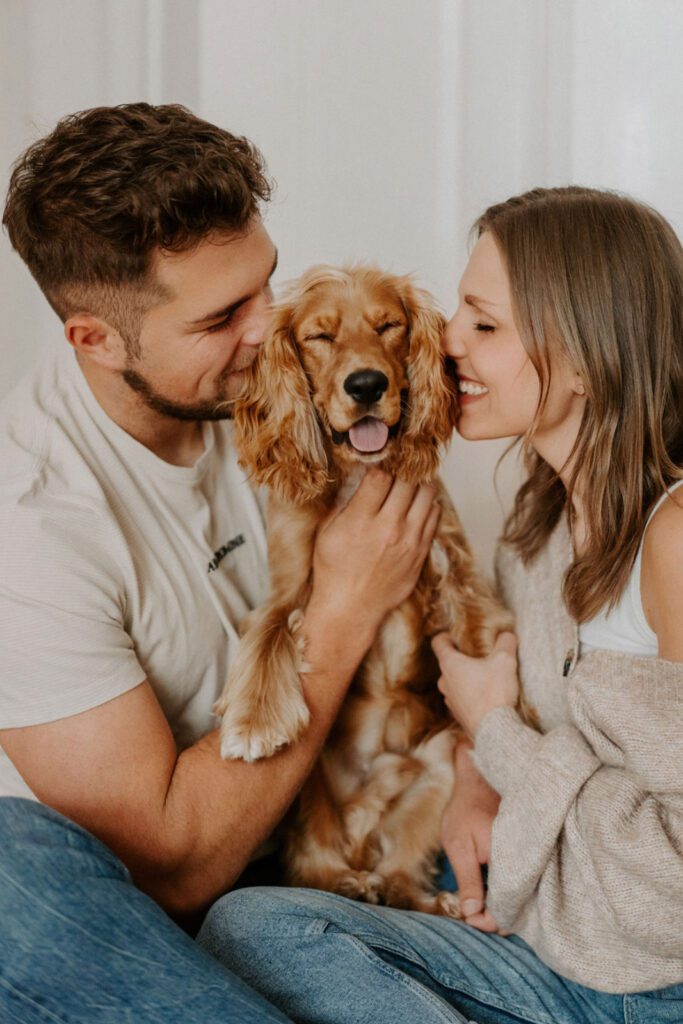 Der rote Englisch Cocker Spaniel Koby grinst zufrieden, während Mama und Papa ihm, während unseres Hundefotoshootings in Berlin, einen Kuss geben.