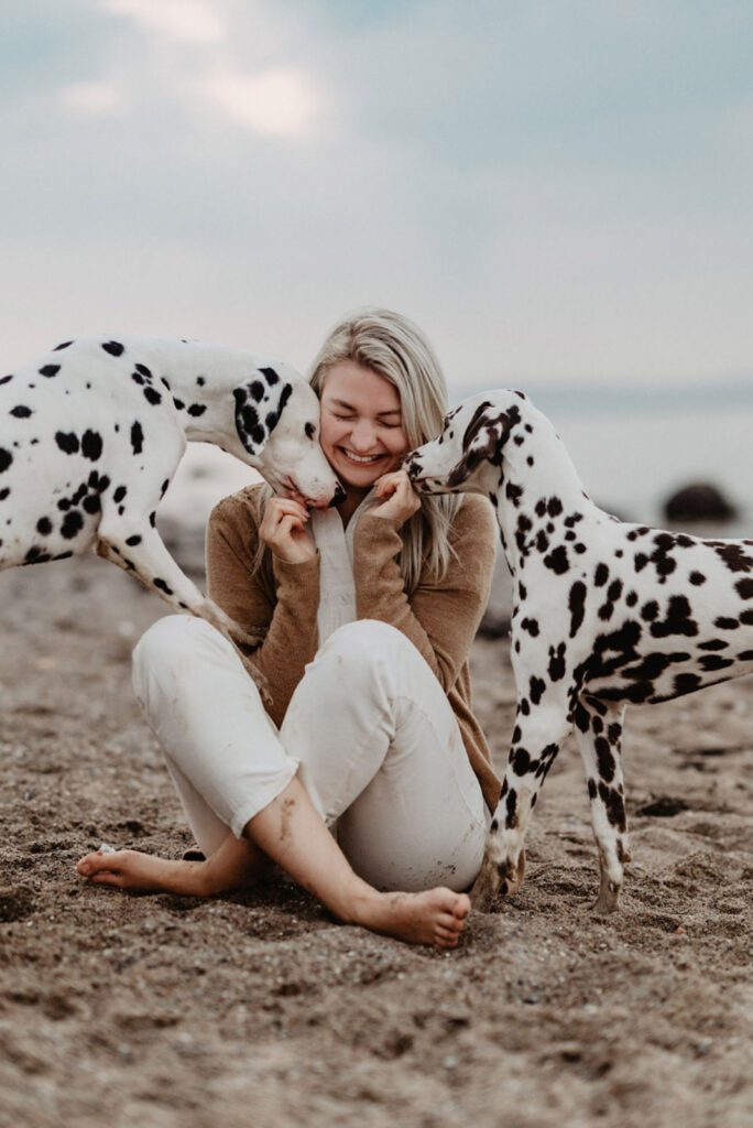 Bei einem Strandshooting geben die beiden Dalmatinerhündinnen ihrem Frauchen einen Hundekuss