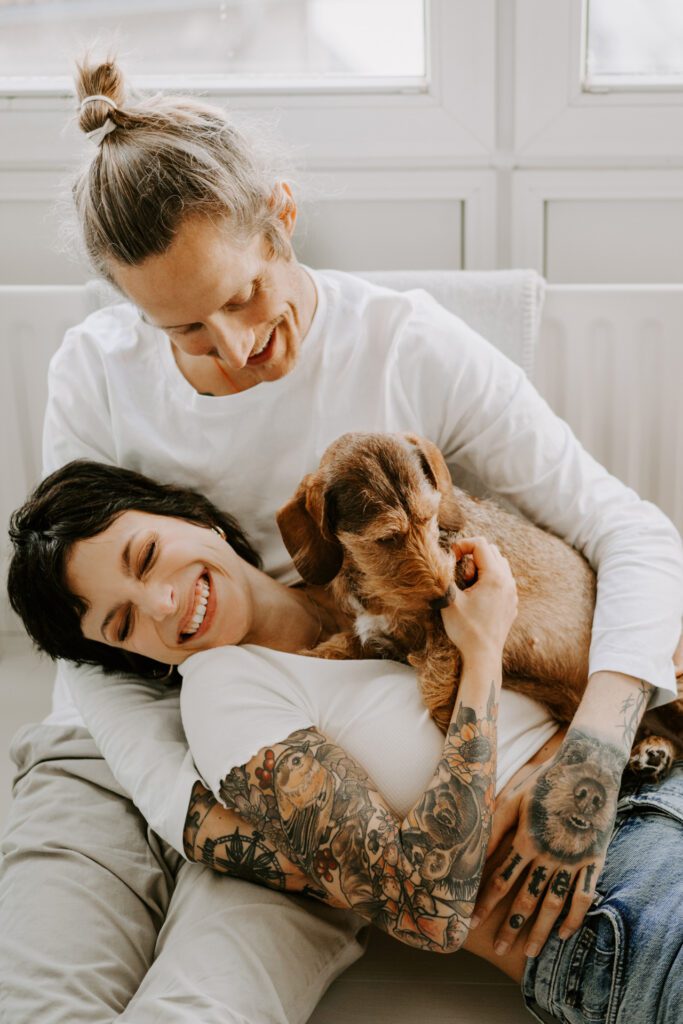 Glückliches junges Paar beim Kuscheln und Lachen mit ihrem Rauhaardackel: Dieses bezaubernde Bild fängt die Liebe und Freude eines jungen Paares ein, das mit ihrem Rauhaardackel lacht. Die herzliche Szene strahlt Wärme und Harmonie aus, während die drei gemeinsam kostbare Momente teilen.